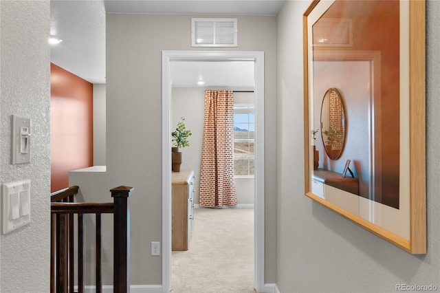 hallway with an upstairs landing, carpet flooring, and visible vents
