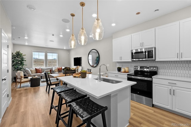 kitchen with decorative backsplash, open floor plan, light wood-type flooring, a sink, and appliances with stainless steel finishes