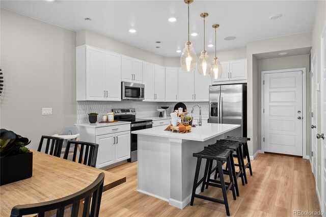 kitchen with stainless steel appliances, tasteful backsplash, white cabinetry, and light wood-style floors