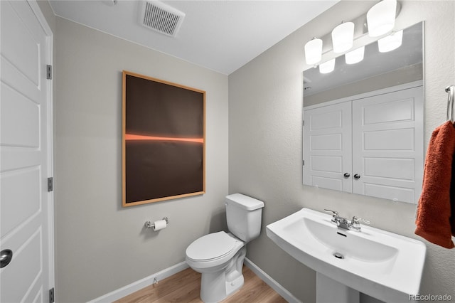 half bathroom featuring visible vents, wood finished floors, a sink, baseboards, and toilet
