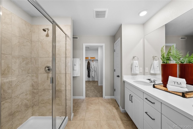 full bath featuring vanity, a walk in closet, a stall shower, and visible vents