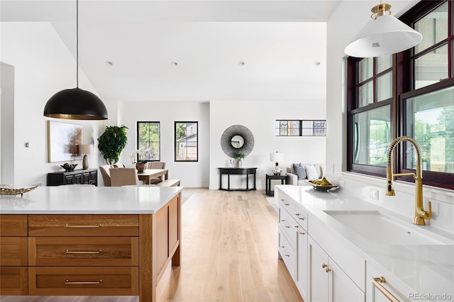 kitchen with sink, white cabinetry, light hardwood / wood-style flooring, and hanging light fixtures