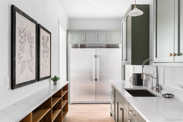 kitchen with built in fridge, light stone countertops, sink, hanging light fixtures, and gray cabinets