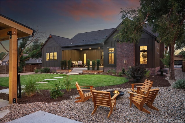 back house at dusk with an outdoor fire pit and a lawn