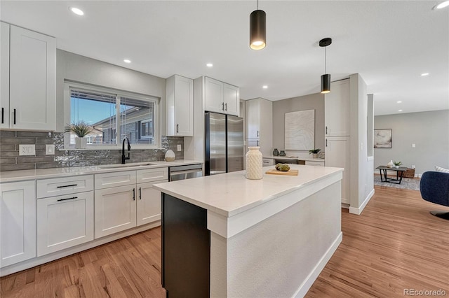 kitchen with light wood finished floors, decorative backsplash, white cabinets, stainless steel appliances, and a sink