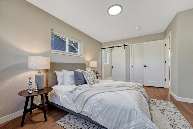 bedroom with a barn door, baseboards, and wood finished floors