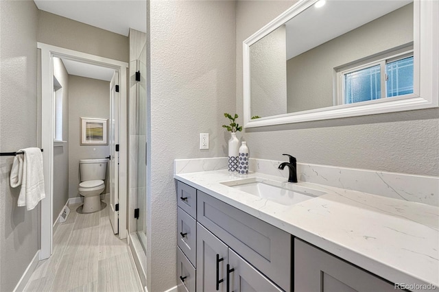 bathroom featuring toilet, a stall shower, wood finished floors, vanity, and a textured wall