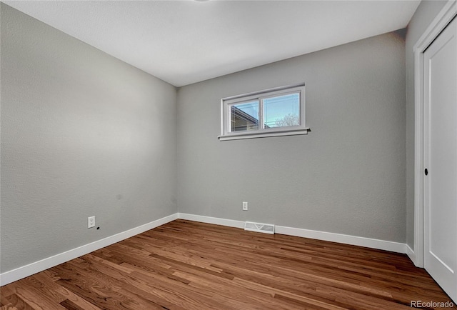 empty room with wood finished floors, visible vents, and baseboards