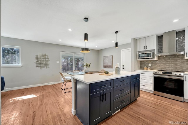 kitchen with wall chimney range hood, backsplash, light wood-style floors, appliances with stainless steel finishes, and light countertops