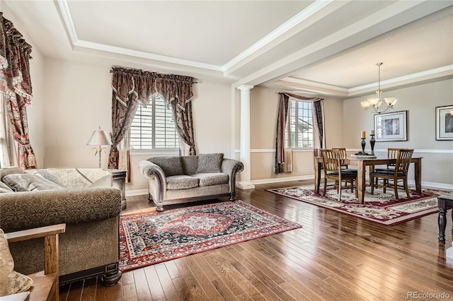 living room with baseboards, wood-type flooring, a tray ceiling, crown molding, and ornate columns