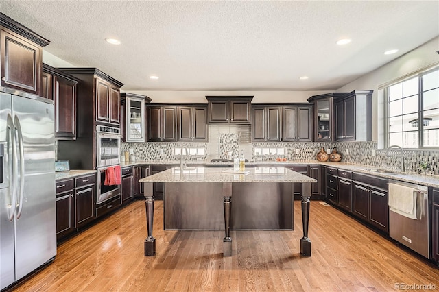 kitchen featuring a center island, a breakfast bar area, stainless steel appliances, light wood-style floors, and a sink