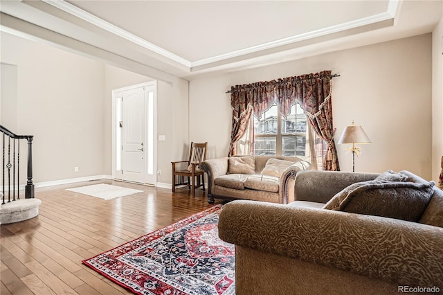 living area with ornamental molding, stairway, wood-type flooring, and a raised ceiling