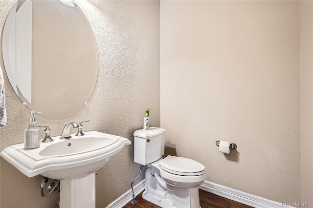 half bath featuring toilet, baseboards, wood finished floors, and a textured wall