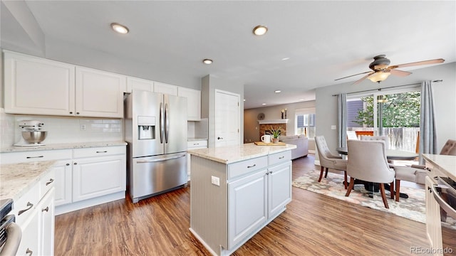 kitchen featuring stainless steel refrigerator with ice dispenser, a kitchen island, wood finished floors, tasteful backsplash, and recessed lighting
