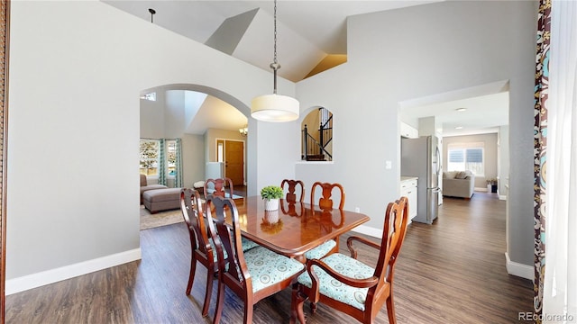 dining space featuring arched walkways, dark wood finished floors, high vaulted ceiling, and baseboards