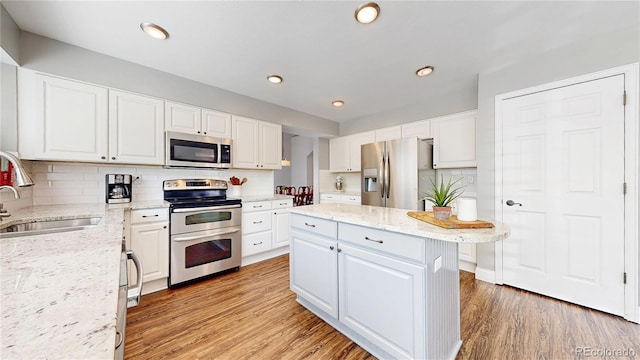 kitchen featuring appliances with stainless steel finishes, a sink, light wood finished floors, decorative backsplash, and white cabinetry