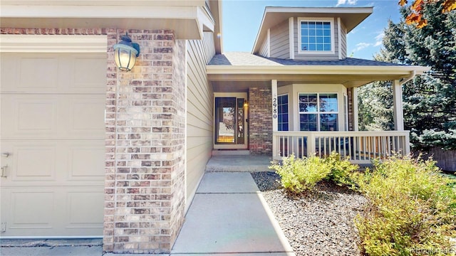entrance to property with a porch, brick siding, an attached garage, and a shingled roof
