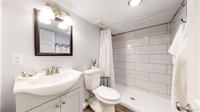 bathroom featuring vanity, toilet, a textured wall, and a tile shower