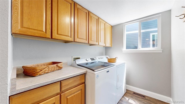 washroom with cabinet space, washing machine and clothes dryer, baseboards, and light wood-style floors