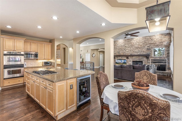 kitchen featuring appliances with stainless steel finishes, dark wood-type flooring, light brown cabinets, a fireplace, and wine cooler