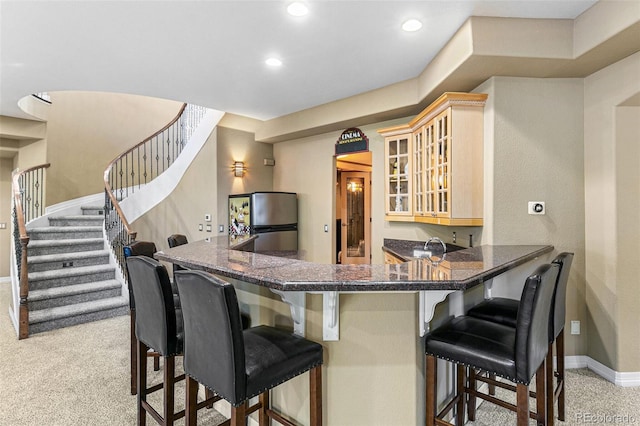 kitchen featuring light carpet, stainless steel fridge, a kitchen bar, and kitchen peninsula