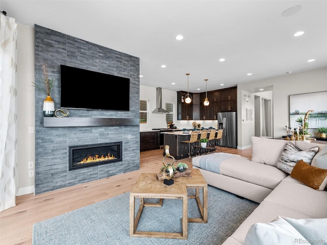 6244 N Lisbon St, Aurora, CO 80019 - living room with light wood-type flooring, recessed lighting, a tiled fireplace, and baseboards