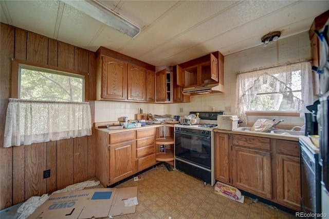 6224 County Road H, Joes, CO 80822 - kitchen featuring black range with gas stovetop, under cabinet range hood, brown cabinets, light countertops, and wood walls