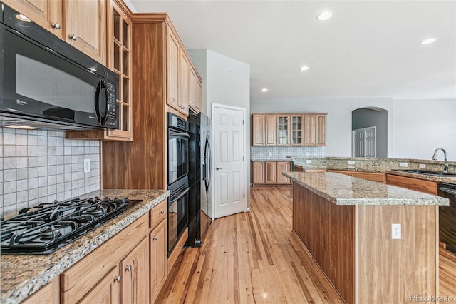 6085 Nile Cir, Golden, CO 80403 - kitchen featuring black appliances, arched walkways, a center island, decorative backsplash, and light wood-type flooring