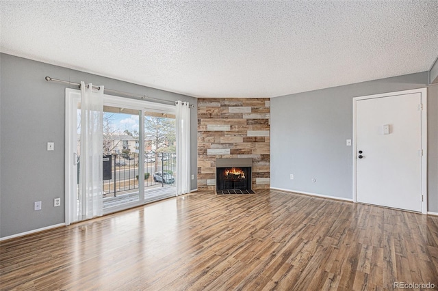 unfurnished living room with a stone fireplace, a textured ceiling, baseboards, and wood finished floors