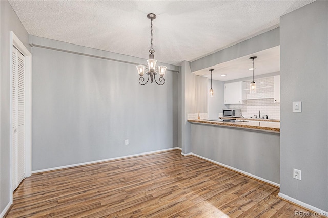 unfurnished dining area with a notable chandelier, a textured ceiling, baseboards, and wood finished floors