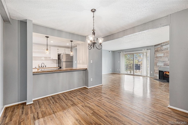 unfurnished living room featuring a chandelier, baseboards, wood finished floors, and a fireplace