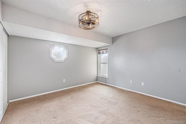 empty room with a notable chandelier, a textured ceiling, baseboards, and carpet floors