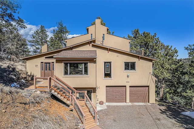 view of front of home featuring an attached garage, stairs, driveway, stucco siding, and a chimney