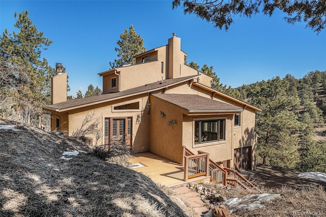 back of property with a shingled roof, a chimney, and stucco siding