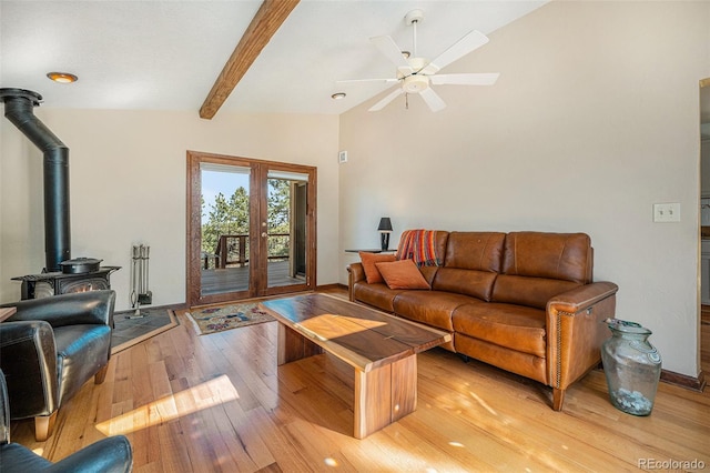 living area featuring a ceiling fan, baseboards, light wood-type flooring, beamed ceiling, and a wood stove