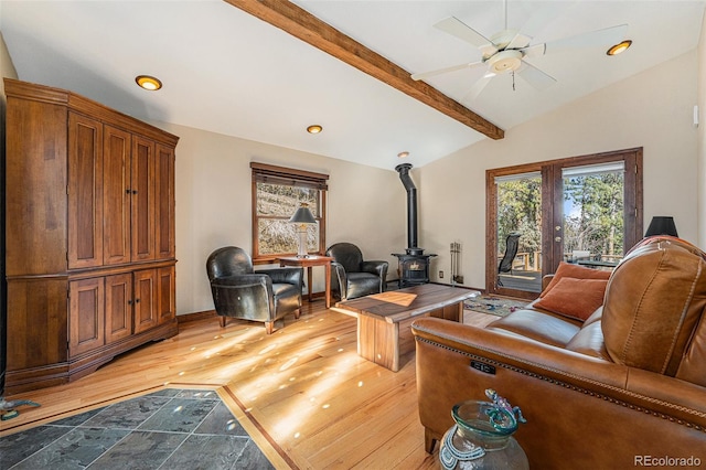 living room with a wood stove, vaulted ceiling with beams, a ceiling fan, and light wood-style floors