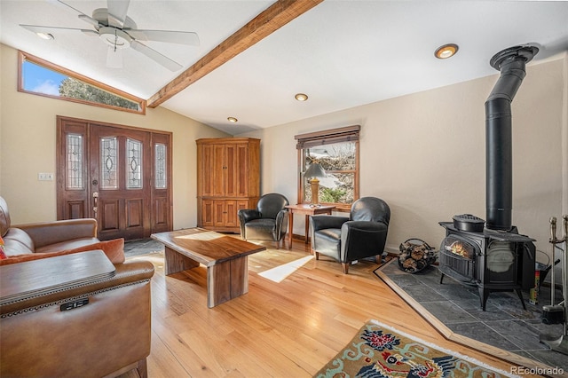 living area with light wood-style floors, a wood stove, vaulted ceiling with beams, and ceiling fan