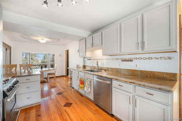 kitchen featuring backsplash, light wood-style flooring, appliances with stainless steel finishes, a sink, and light stone countertops