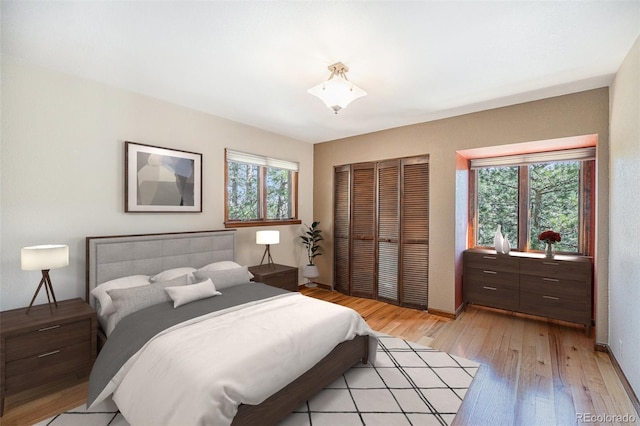 bedroom featuring light wood finished floors, multiple windows, baseboards, and a closet