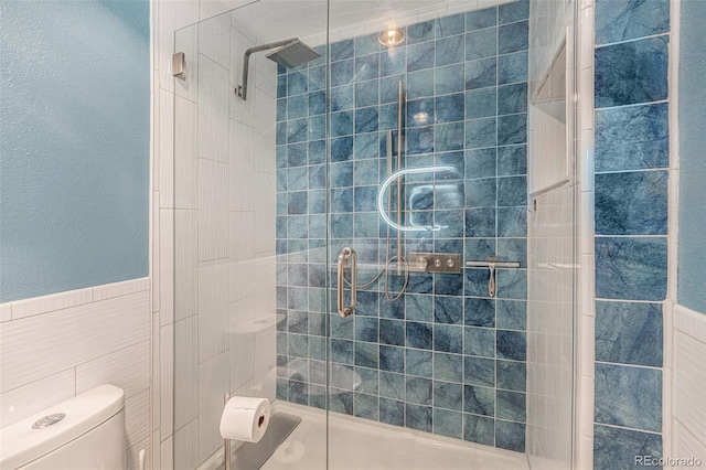 bathroom featuring a stall shower, wainscoting, toilet, and tile walls