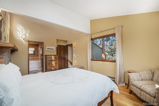 bedroom with lofted ceiling, connected bathroom, baseboard heating, and wood finished floors