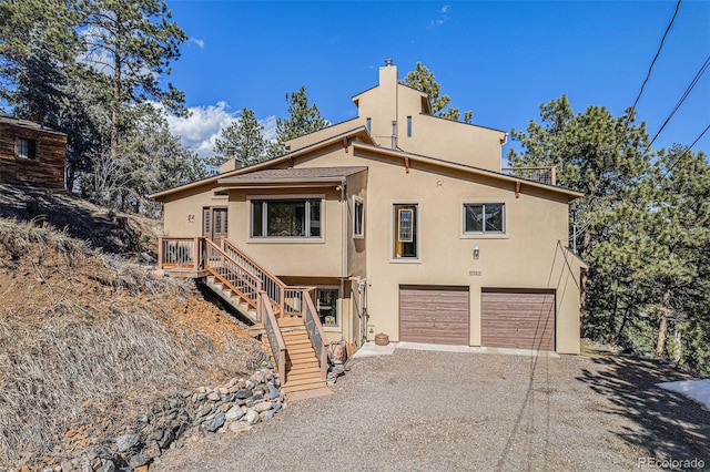 view of front facade featuring a chimney, stucco siding, stairway, a garage, and driveway