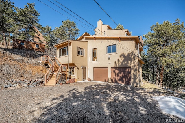 exterior space featuring a chimney, stucco siding, stairway, a garage, and driveway