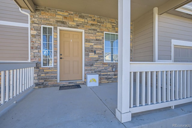 view of exterior entry with stone siding and covered porch