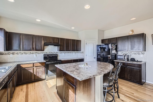 kitchen with light wood-style flooring, a breakfast bar, a center island, under cabinet range hood, and black appliances