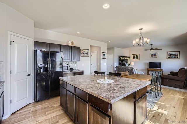 kitchen featuring a center island, decorative light fixtures, black refrigerator with ice dispenser, open floor plan, and light wood-type flooring