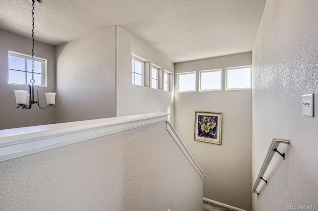 stairway featuring a textured ceiling, a textured wall, and an inviting chandelier