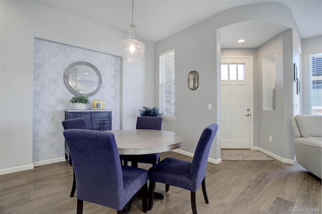 dining area featuring arched walkways, baseboards, and wood finished floors