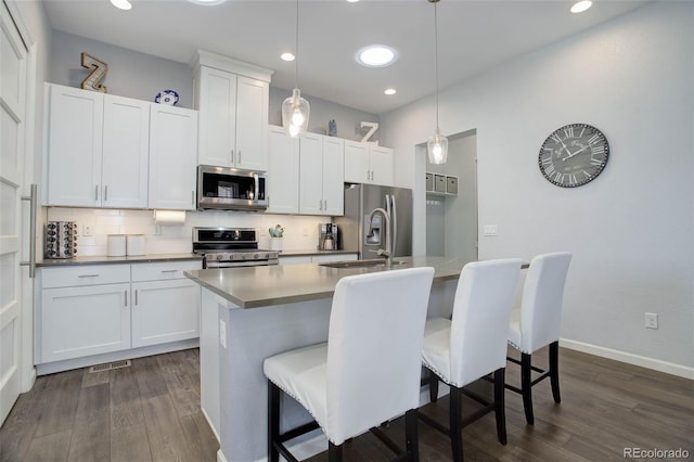 kitchen featuring dark wood-type flooring, an island with sink, tasteful backsplash, and stainless steel appliances