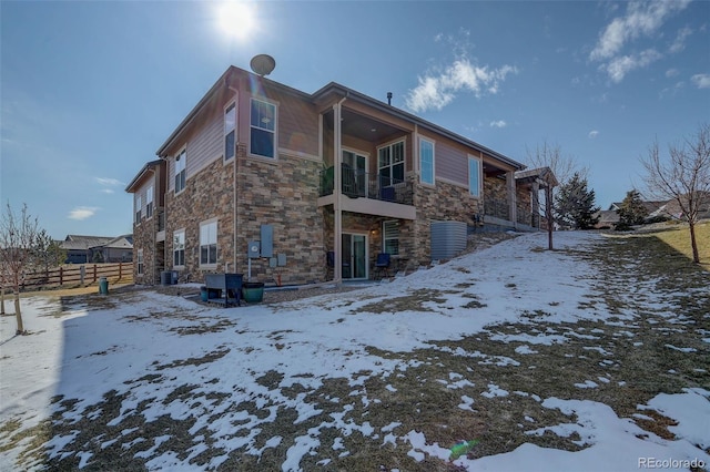 view of snowy exterior with central AC unit, a balcony, fence, and stone siding